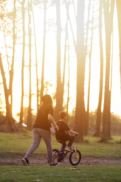 Photo mother helping son to ride bicycle during sunset