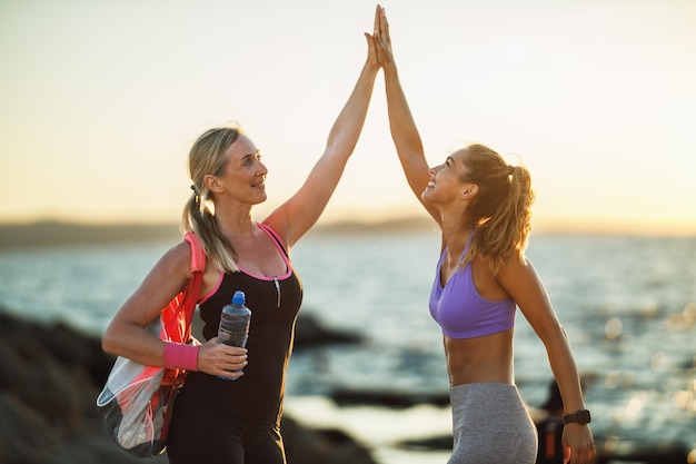 Mother and her adult daughter giving high five and support each other during training near the sea beach.