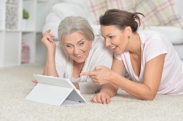 Mother and her adult daughter lying on floor and looking at tabl