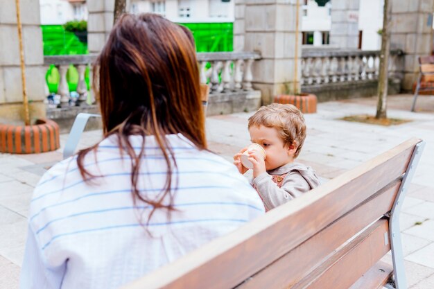 放課後の午後にアイスクリームを食べることを楽しんでいる彼女の3歳の息子と彼女の背中に母親