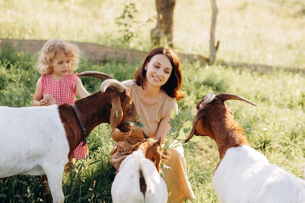 Foto una madre e la sua bellissima figlia riccia pascolano le capre in una fattoria ecologica