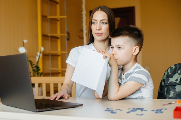 母親と子供は、自宅のコンピューターの前で遠隔教育に従事しています。外出禁止令、トレーニング。