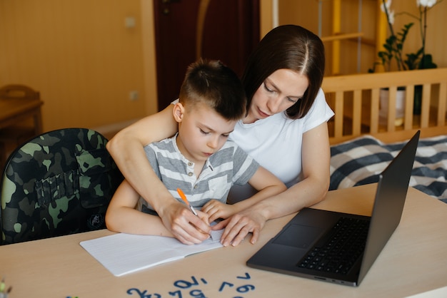 母親と子供は自宅のコンピューターの前で遠隔学習に従事しています。家にいる、トレーニングする。