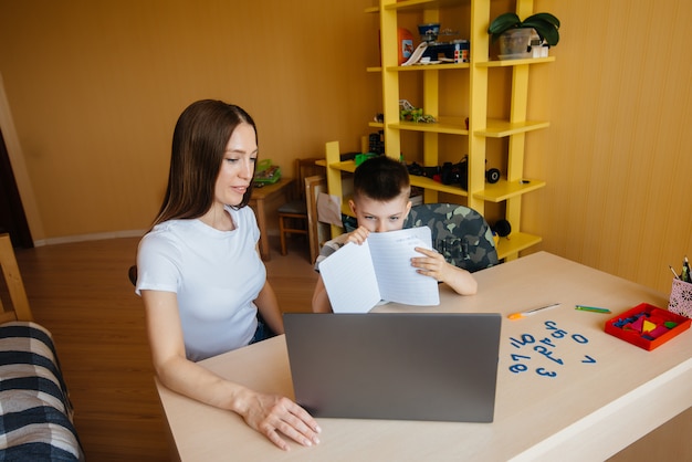 母親と子供は自宅のコンピューターの前で遠隔学習に従事しています。家にいる、トレーニングする。