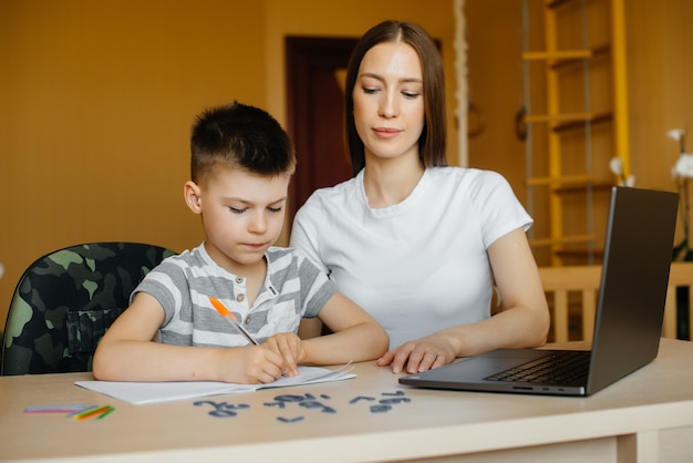 母親と子供は自宅のコンピューターの前で遠隔学習に従事しています。家にいる、トレーニングする。