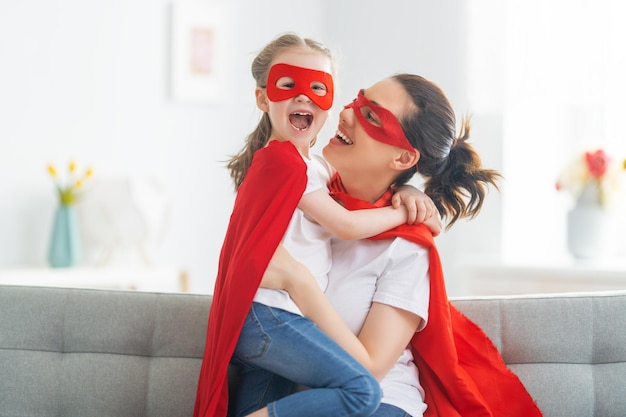 Mother and her child playing together Girl and mom in Superhero costume