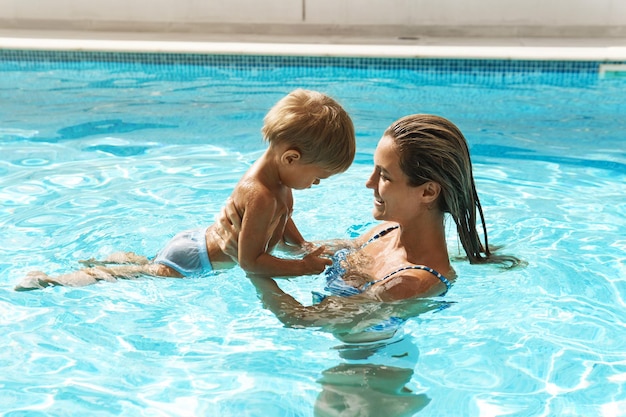 Мать и ее милый маленький сын плавают в открытом бассейне во время летних каникул
