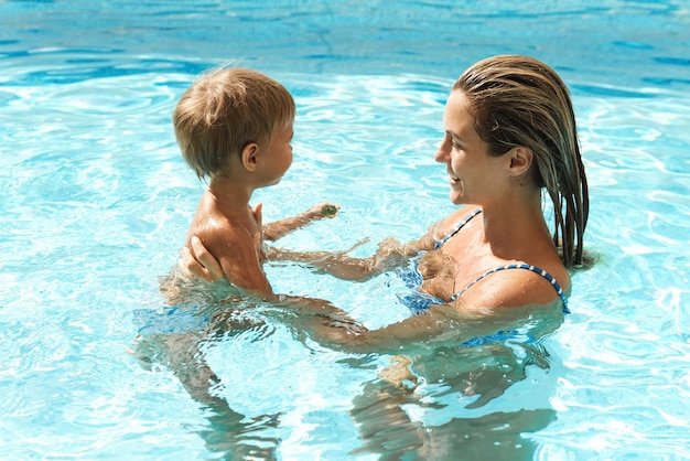 Mother and her cute little son swimming in outdoor pool during summer vacation