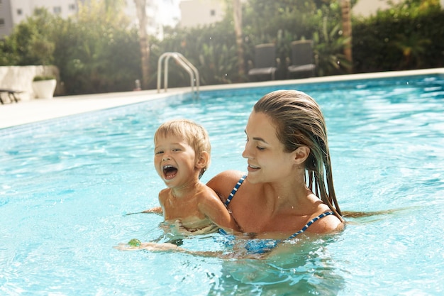 Mother and her cute little son swimming in outdoor pool during summer vacation