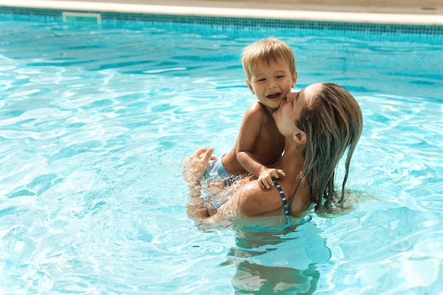 Мать и ее милый маленький сын плавают в открытом бассейне во время летних каникул