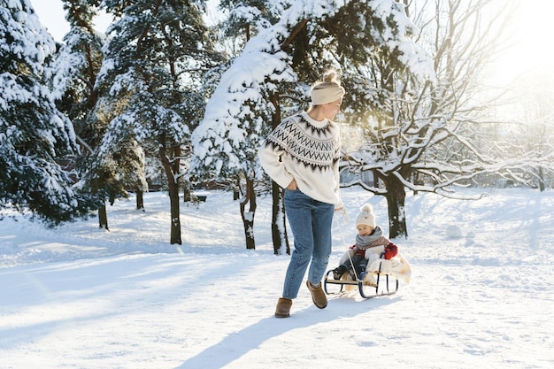 Mother and her cute little son wearing warm sweaters are having on a sledding hill during sunny winter day