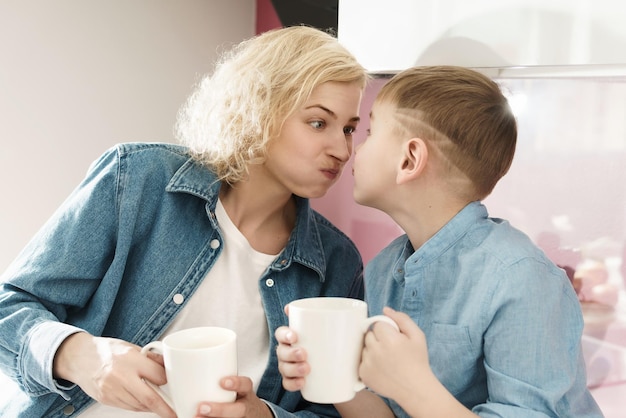 Mother and her cute son are drinking tea and making silly faces during the breakfast