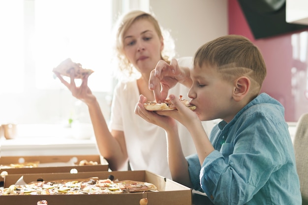 Mother and her cute son eating delicious Italian pizza at home