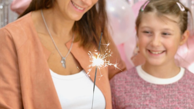 母と彼女の娘は誕生日パーティーで線香花火が燃えるのを見ています