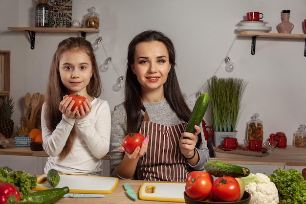 Мать и дочь готовят овощной салат и веселятся на кухне.