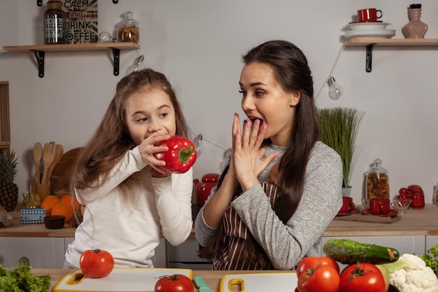 Мать и дочь готовят овощной салат и веселятся на кухне.