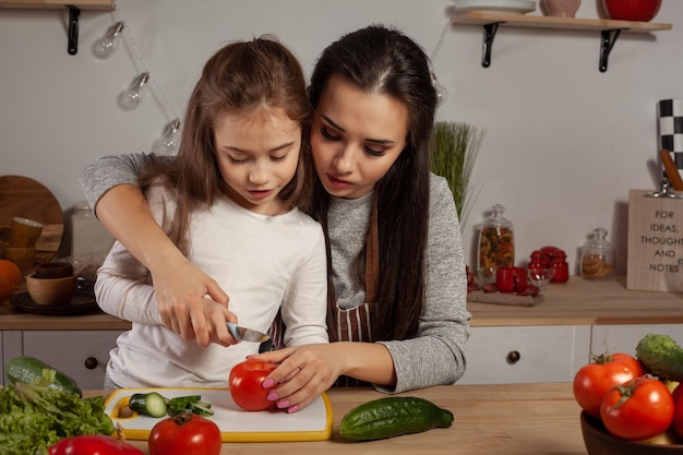 Мать и дочь готовят овощной салат и веселятся на кухне.