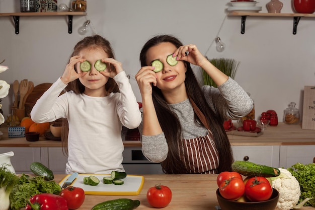 Мать и дочь готовят овощной салат и веселятся на кухне.