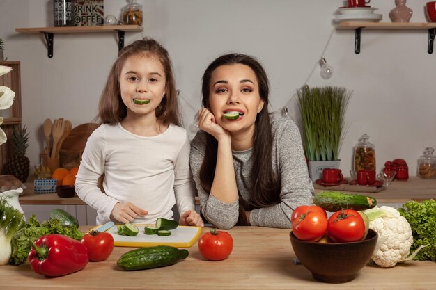 Мать и дочь готовят овощной салат и веселятся на кухне.