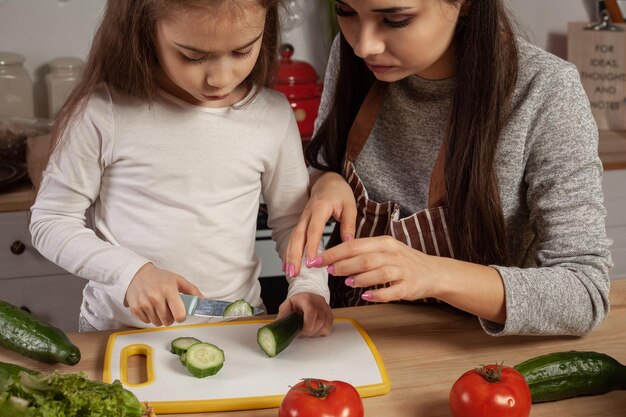 Mother and her daughter are making a vegetable salad and having fun at the kitchen.