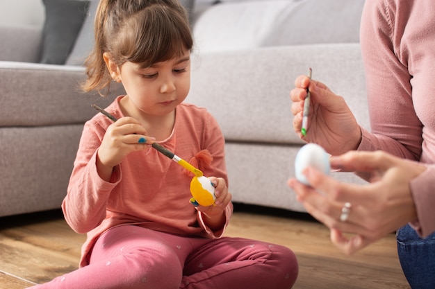 A mother and her daughter painting Easter eggs at home.