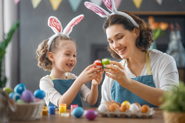 Mother and her daughter painting eggs Cute little child girl wearing bunny ears