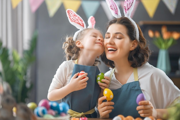 Mother and her daughter painting eggs Happy family preparing for Easter wearing bunny ears