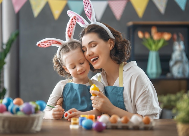 Mother and her daughter painting eggs Happy family preparing for Easter