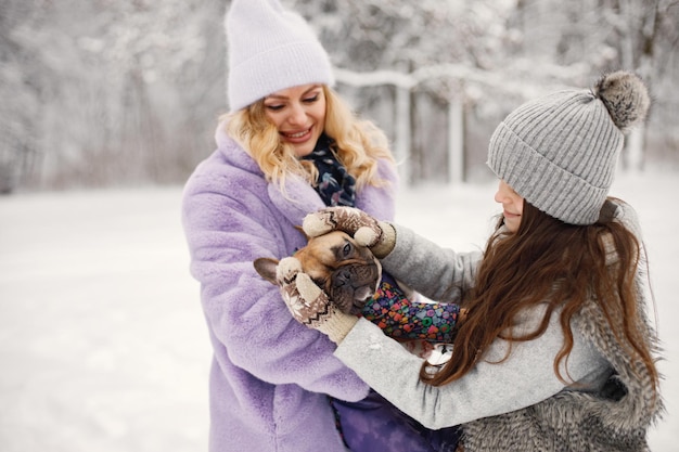 Мать и ее дочь играют со своей собакой французским бульдогом на снегу