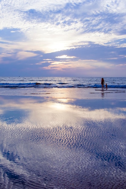 Мать и ее ребенок стоят на пляже Потрясающее небо отражается в море