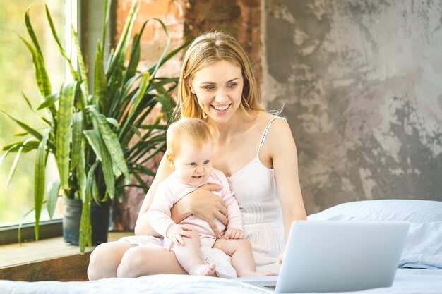 Mother and her little baby at home. Mother with her baby watching something on laptop.