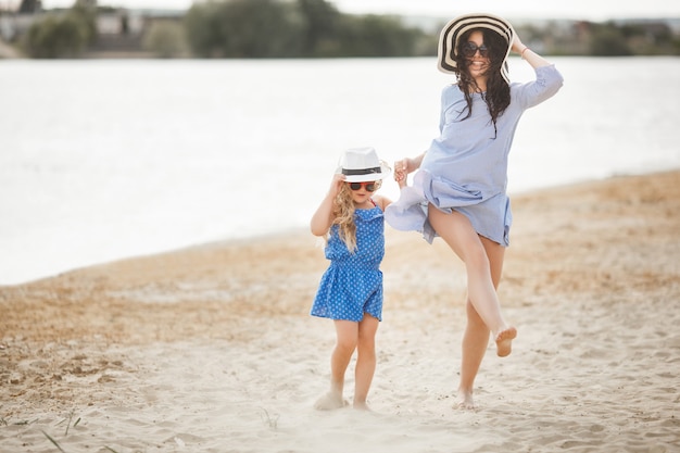 母と彼女の小さな娘が海岸で楽しんでいます。若い可愛いお母さんと彼女の子供が水の近くで遊んで