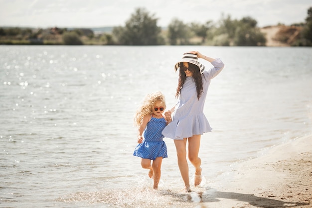 Mother and her little daughter having fun at the coast. Young pretty mom and her child playing near the water