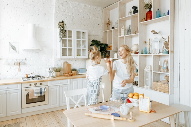 A mother and her little daughter prepare baking dough together in their kitchen at home.