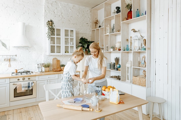 A mother and her little daughter prepare baking dough together in their kitchen at home.