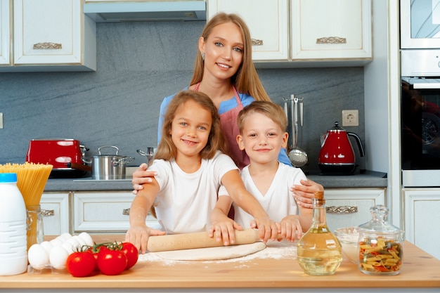 Mother and her little kids, boy and girl, helping her to prepare dough 