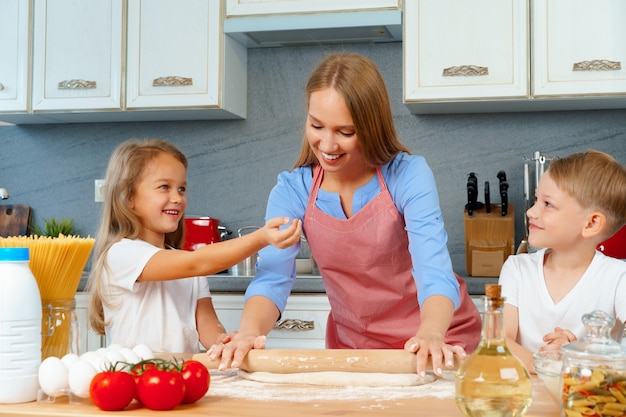 Mother and her little kids, boy and girl, helping her to prepare dough 