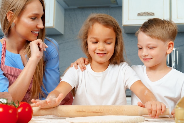 Mother and her little kids helping her to prepare dough