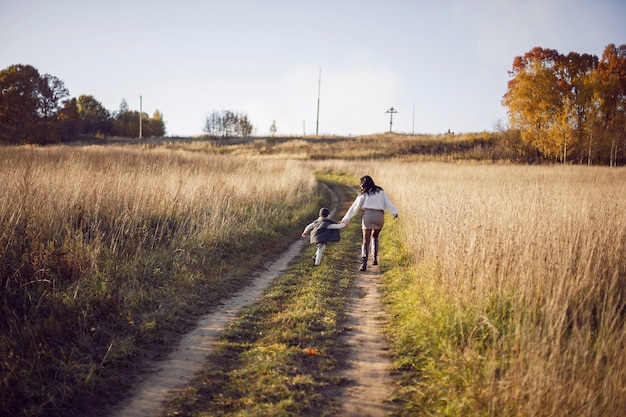 Mother and her son are run in a field with dry grass at sunset