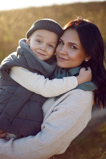 Photo mother and her son are standing in a field with dry grass at sunset in autumn