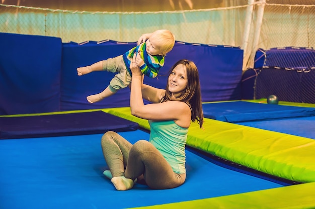 Mother and her son jumping on a trampoline in fitness park and doing exersice indoors