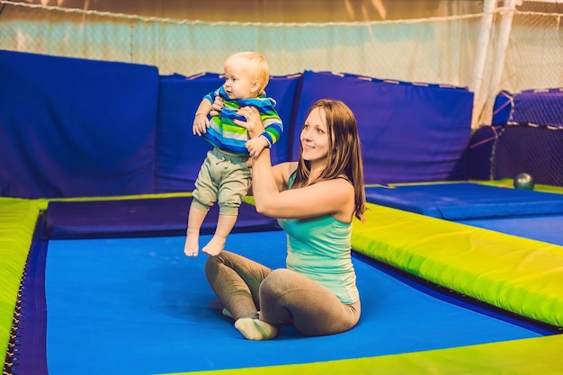 Mother And her son jumping on a trampoline in fitness park and doing exersice indoors