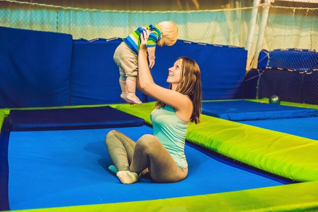 Mother And her son jumping on a trampoline in fitness park and doing exersice indoors