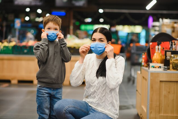 Mother and her son wearing protective face mask shop at a supermarket during the coronavirus epidemic