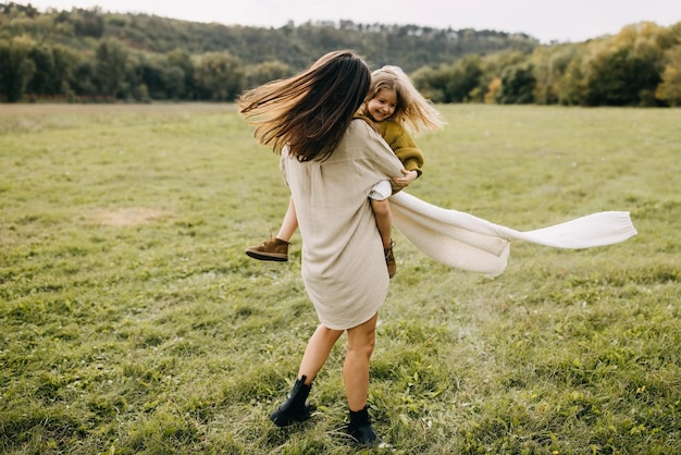 Mother and her toddler daughter playing outdoors dancing in a field with green grass