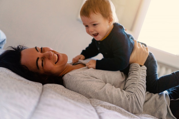 Photo mother and his son playing on the bed at home