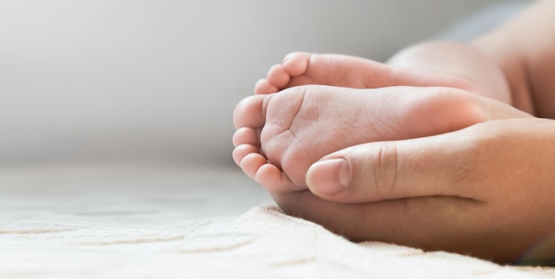 Madre che tiene i piedi del bambino nelle mani. gambe neonato in genitori di sesso femminile mano. i piedi dei bambini piccoli nel palmo della mamma. avvicinamento. dita dei piedi del bambino e mani della donna del genitore felice. festa della mamma