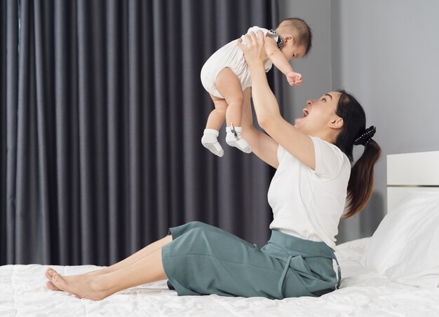 그녀의 팔에 아기 신생아를 안고 집에서 침대에 들어 올리는 어머니