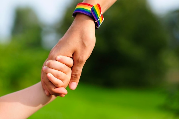 мать держит ребенка за руку. ЛГБТ радужный браслет на руке родителей
