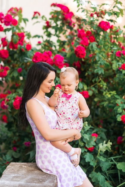 Madre che tiene in braccio la figlia su uno sfondo di rose rosse